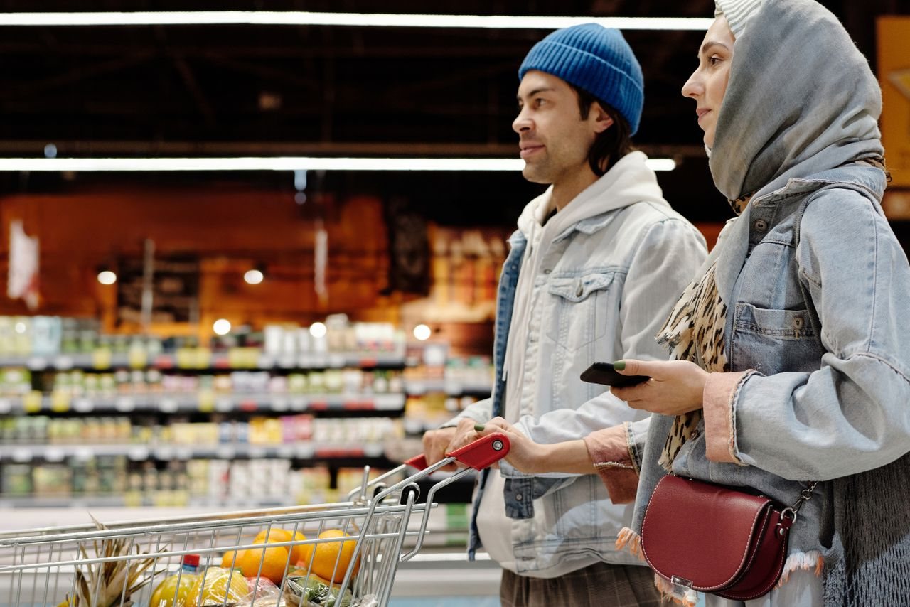 Free A young couple shopping with a cart in a supermarket aisle, selecting fresh produce. Stock Photo